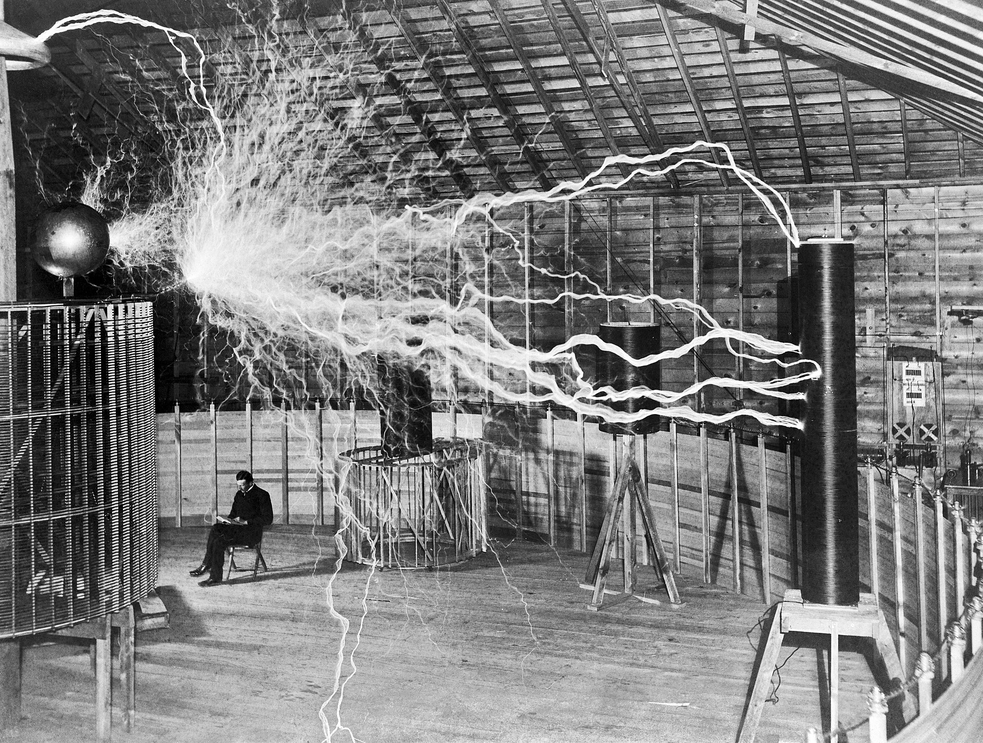 Nikola Tesla seated in his Colorado Springs laboratory beneath his magnifying transmitter, producing large electrical arcs